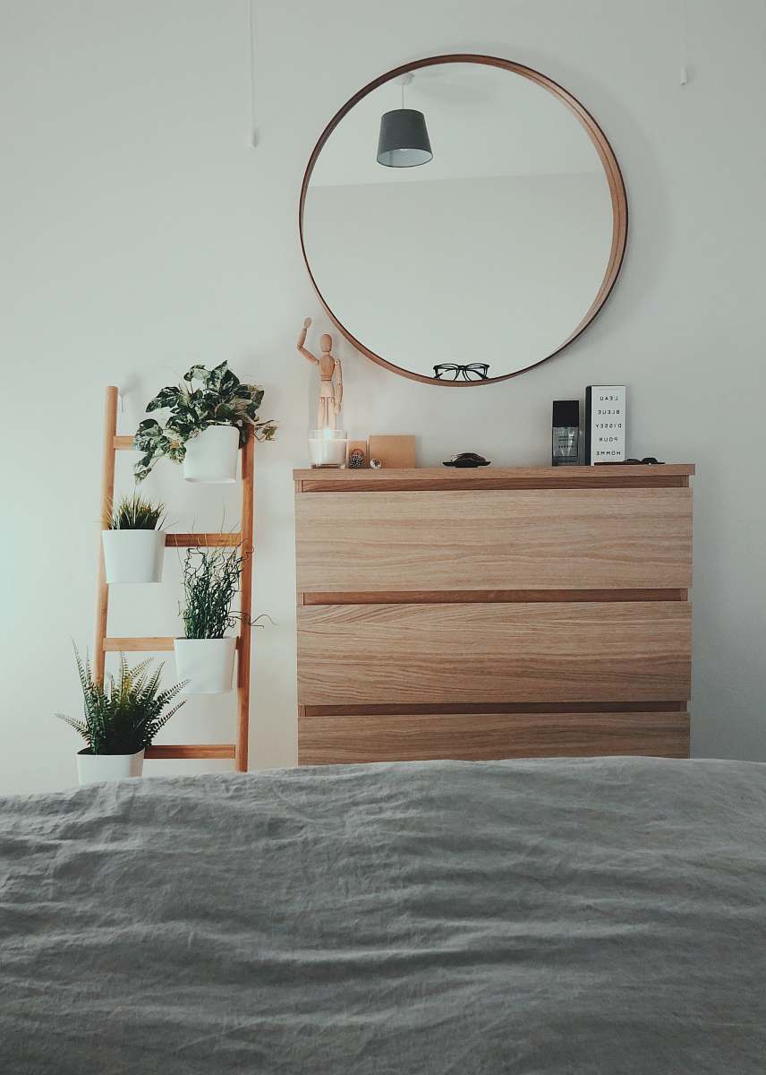 potted plant brown wooden 3-drawer chest with round brown wooden framed mirror in front of bed inside room plant